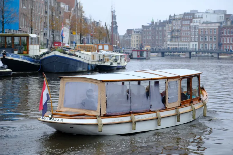 Sightseeing boat cruising an Amsterdam canal with historic canal houses behind
