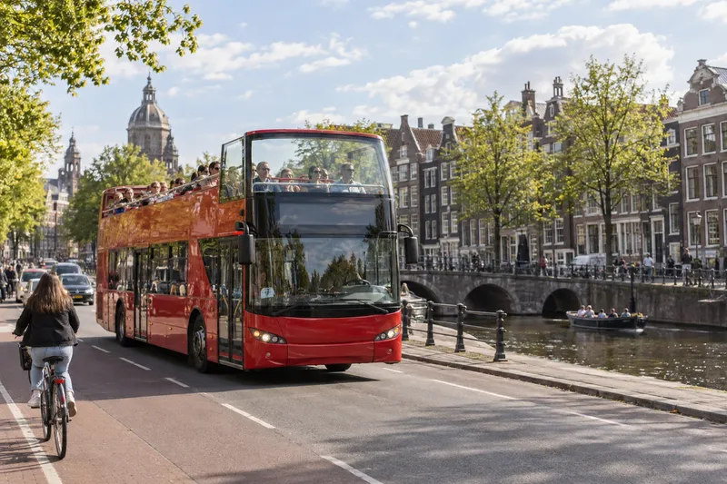 Red hop-on hop-off sightseeing bus beside an Amsterdam canal