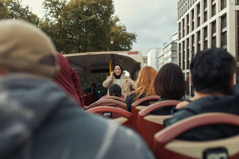 Passengers riding an open-top sightseeing bus through a city street