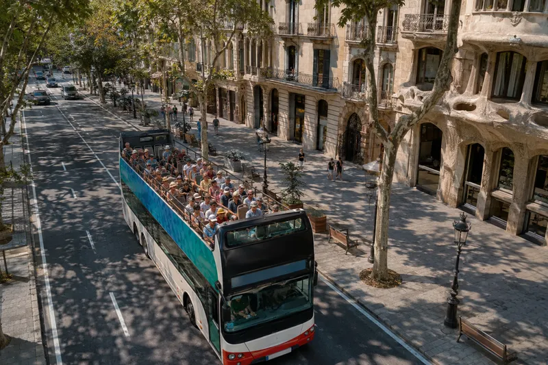 Open-top sightseeing bus driving along a tree-lined street in central Barcelona