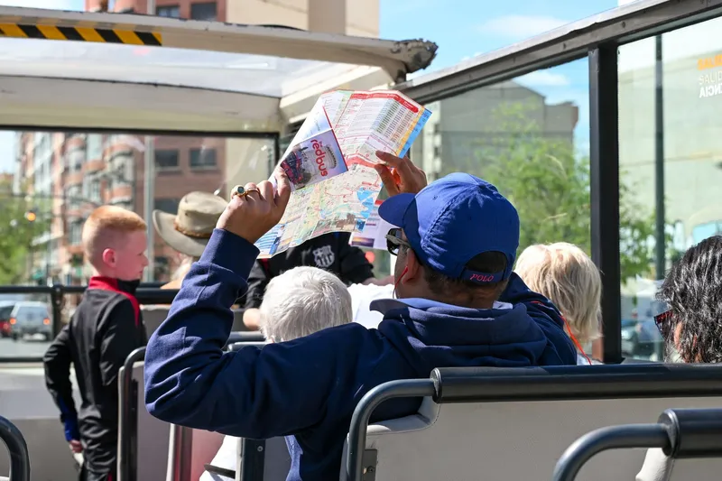 Passengers riding an open-top double-decker sightseeing bus through the city