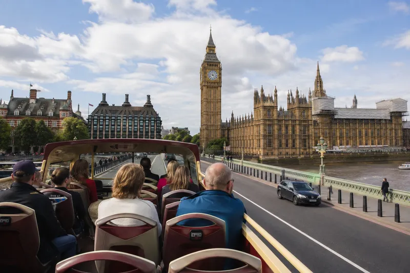 Passengers on an open-top sightseeing bus passing Big Ben and the Houses of Parliament in London