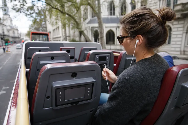 Passenger using an audio guide on an open-top double-decker sightseeing bus