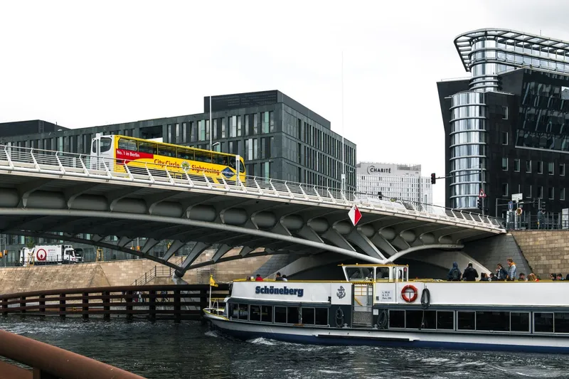 Open-top sightseeing bus on bridge above river cruise boat on urban river