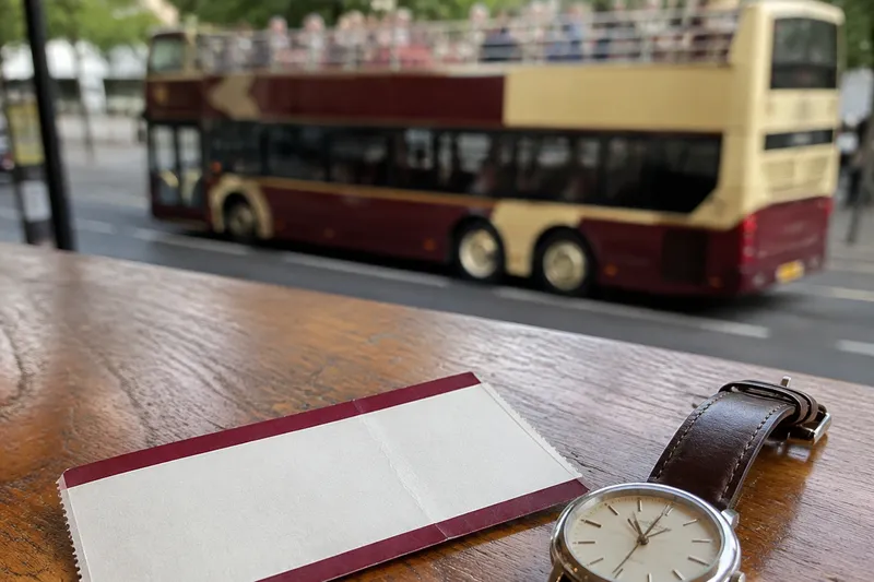 Paper sightseeing ticket and analog wristwatch on a table with a sightseeing bus outside