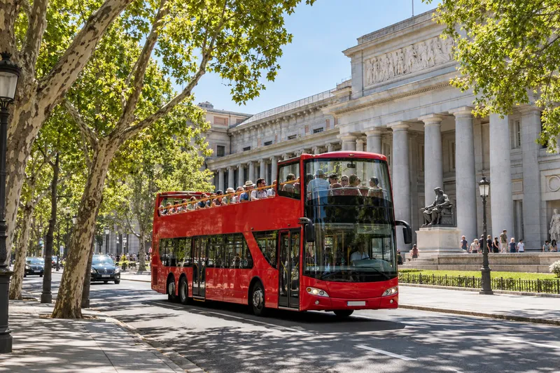 Red open-top sightseeing bus on Paseo del Prado in Madrid by the Prado Museum