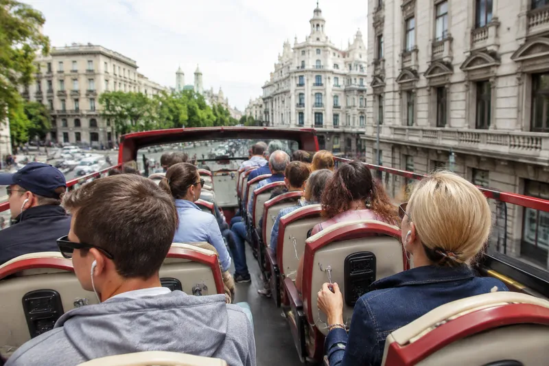 Passengers on a red open-top double-decker sightseeing bus in a European city