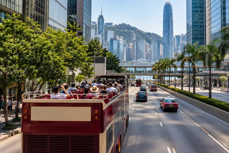 Open-top sightseeing bus driving through Hong Kong with skyscrapers and Victoria Harbour