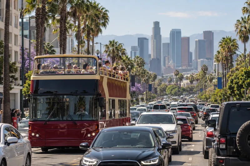Open-top double-decker Los Angeles tour bus in heavy traffic with downtown skyline