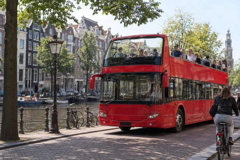 Red open-top double-decker sightseeing bus on a canal street in Amsterdam