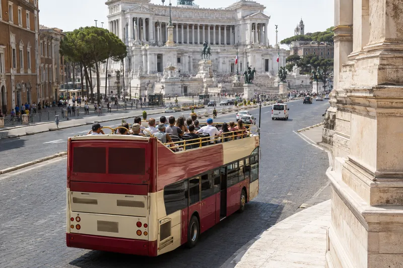 Open-top sightseeing bus passing Rome's historic center near the Vittoriano monument