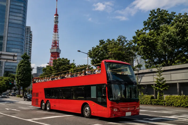 Open-top double-decker sightseeing bus driving through central Tokyo with Tokyo Tower in the background