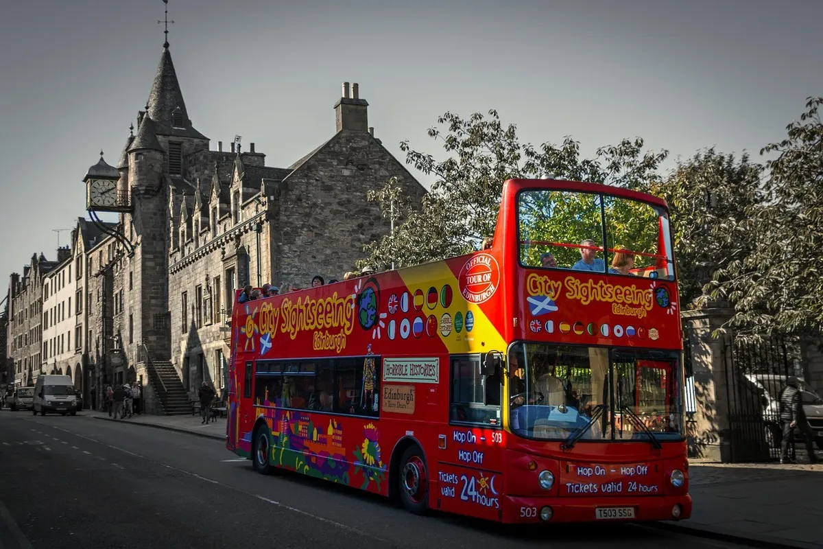 Open-top double-decker sightseeing bus on a historic Edinburgh city street