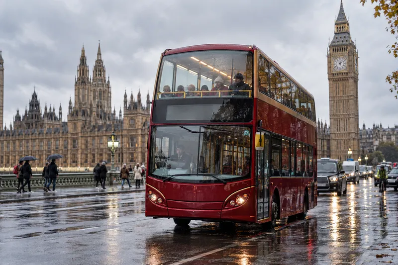 Red double-decker sightseeing bus crossing Westminster Bridge in London in the rain